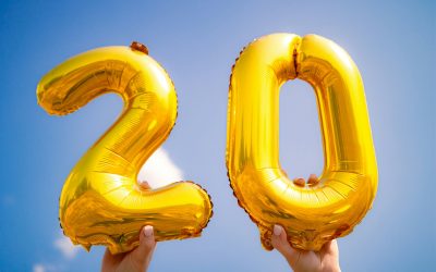 Hands holding up two balloons, a 2 and a 0.