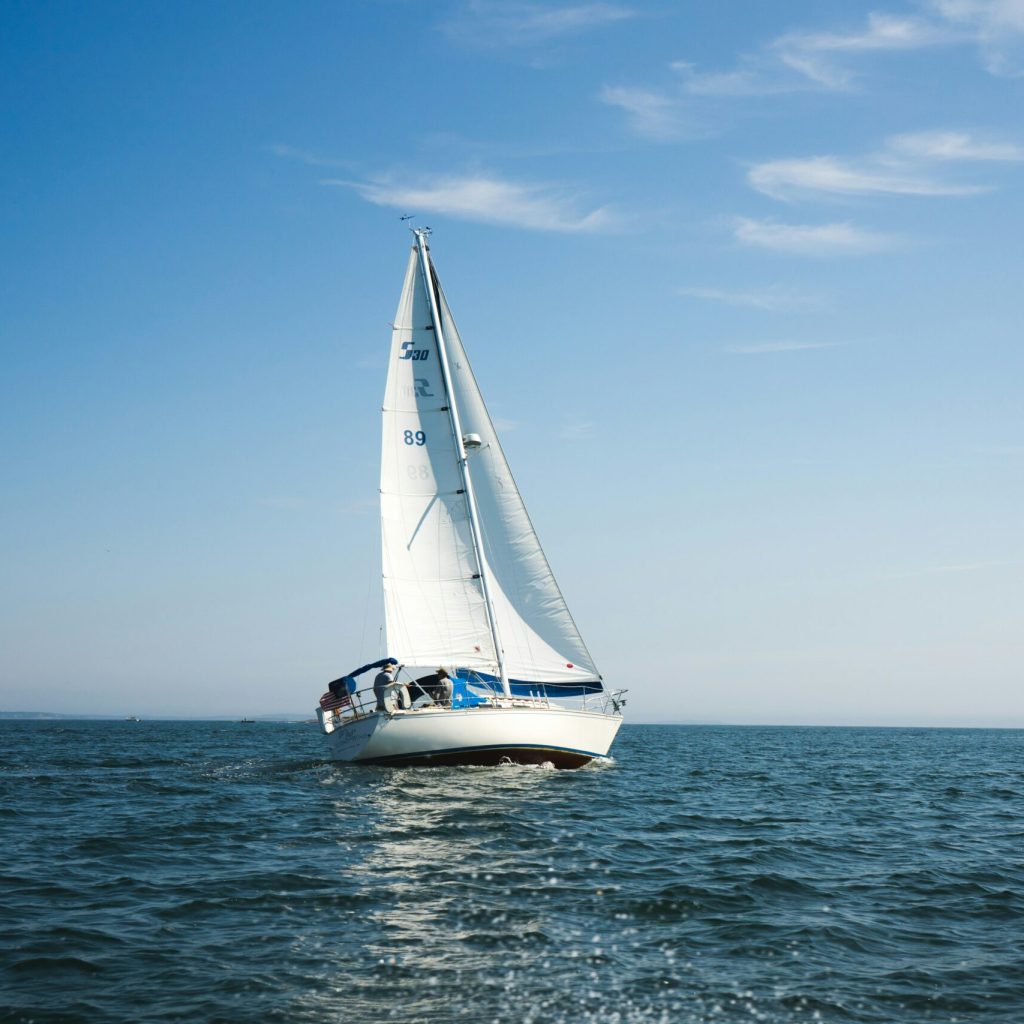 A white sailboat in the middle of the picture, with a clear blue sky and dark blue water.