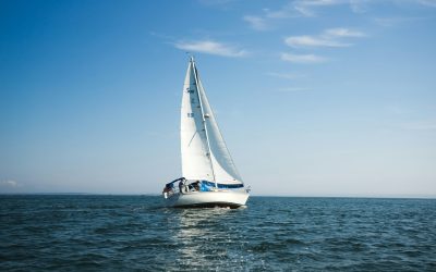 A white sailboat in the middle of the picture, with a clear blue sky and dark blue water.